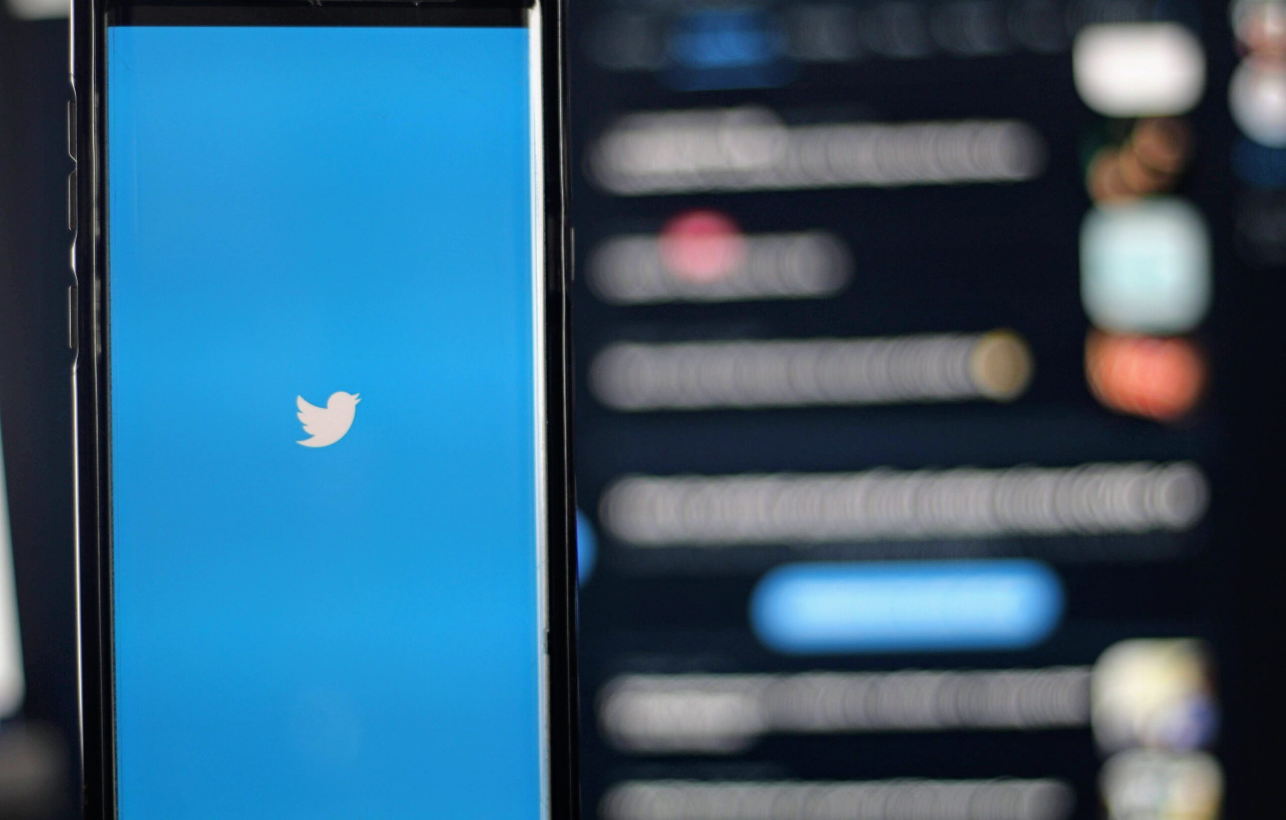 phone showing twitter logo with twitter timeline on a screen in background